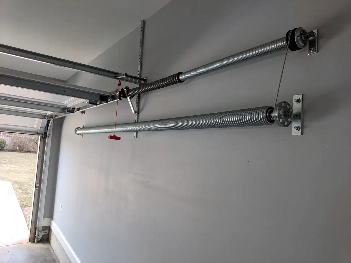 Two garage door torsion springs are mounted on a light gray wall.